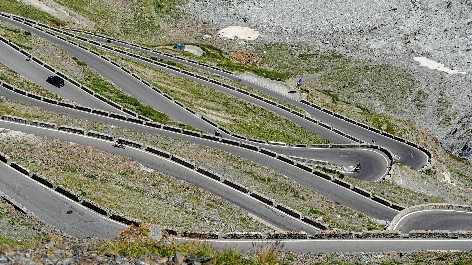 Aerial view of a winding mountain road with cyclists and a vehicle navigating sharp turns.