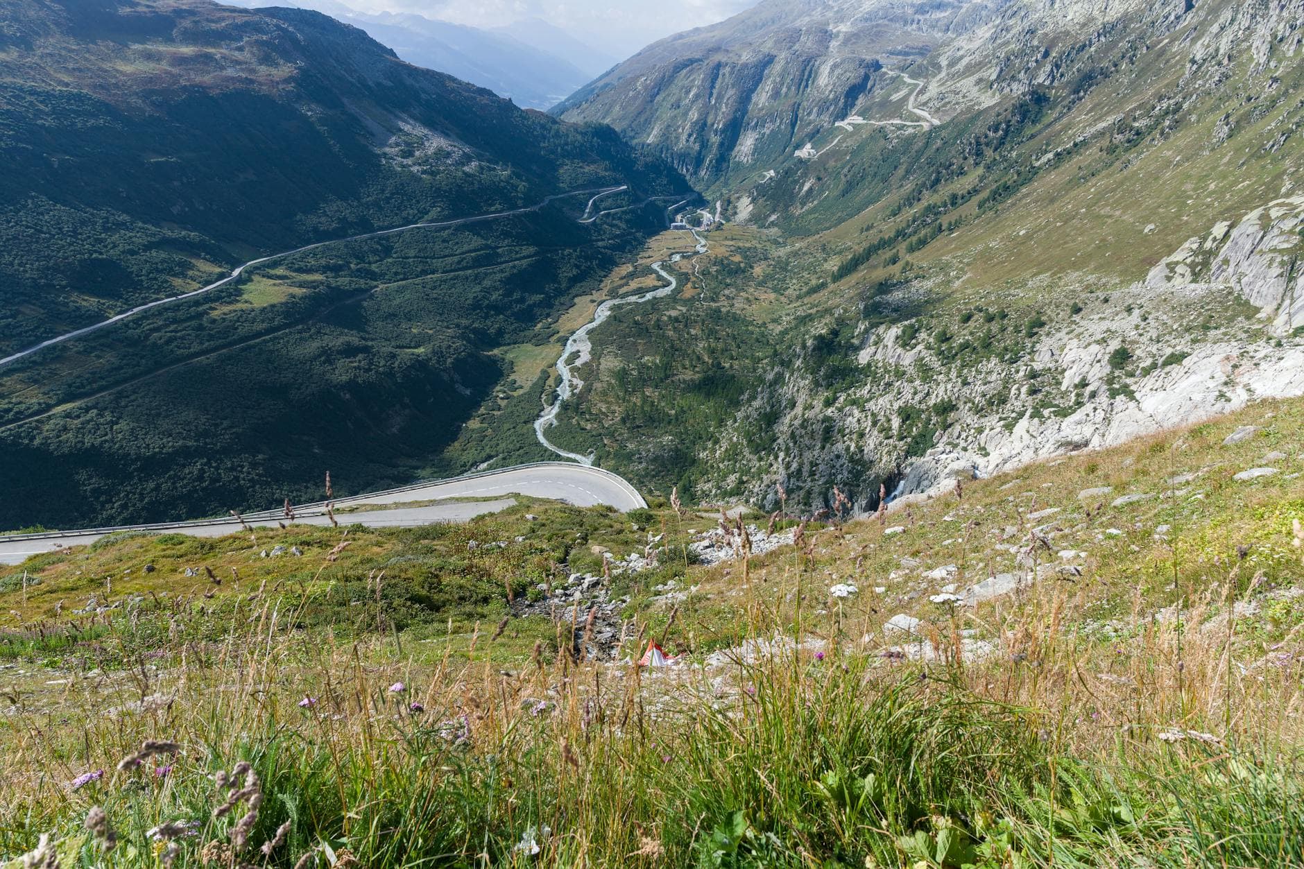 Beautiful panoramic view of the Swiss Alps with winding roads and lush valleys under a clear sky.