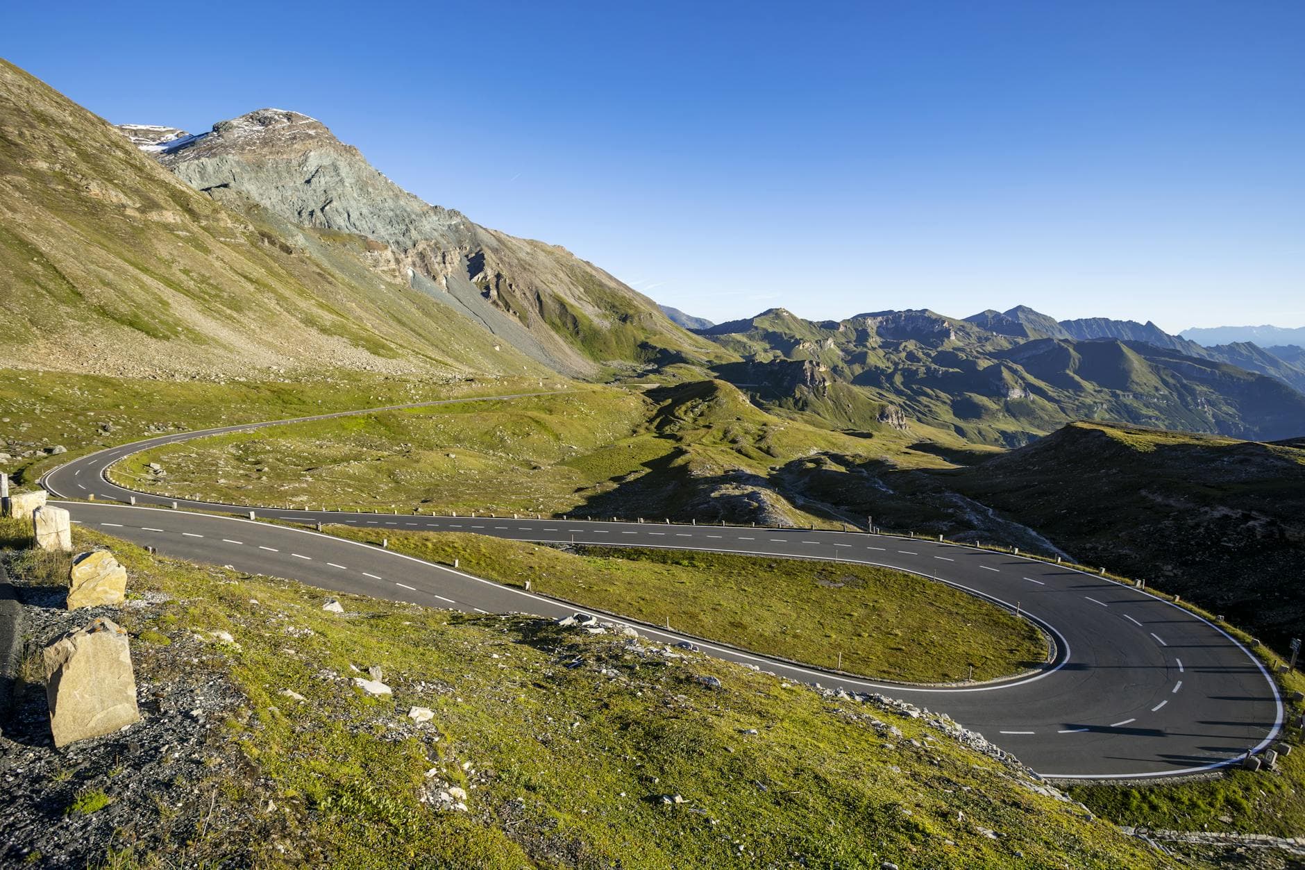 A winding road through picturesque mountain landscape under a clear blue sky.