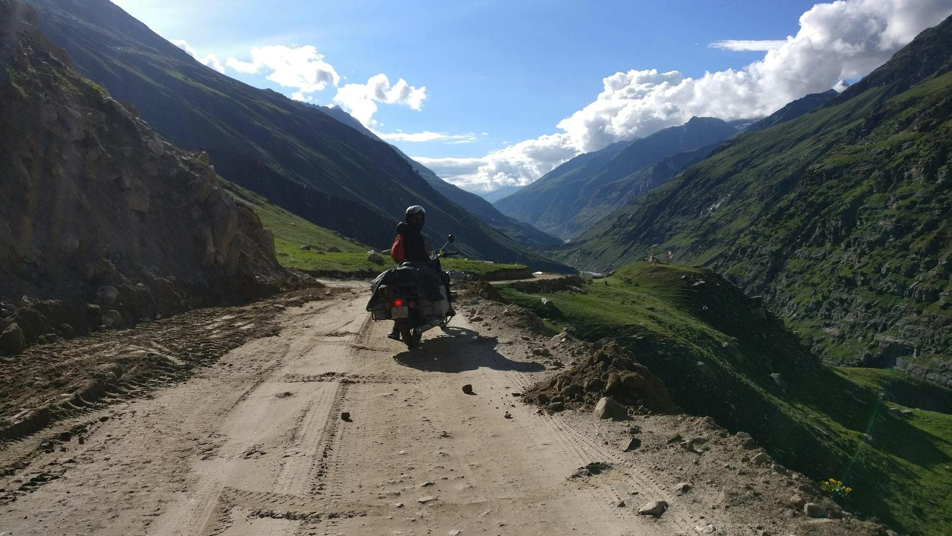 A solo motorcyclist navigates a rugged mountain road under a clear blue sky.