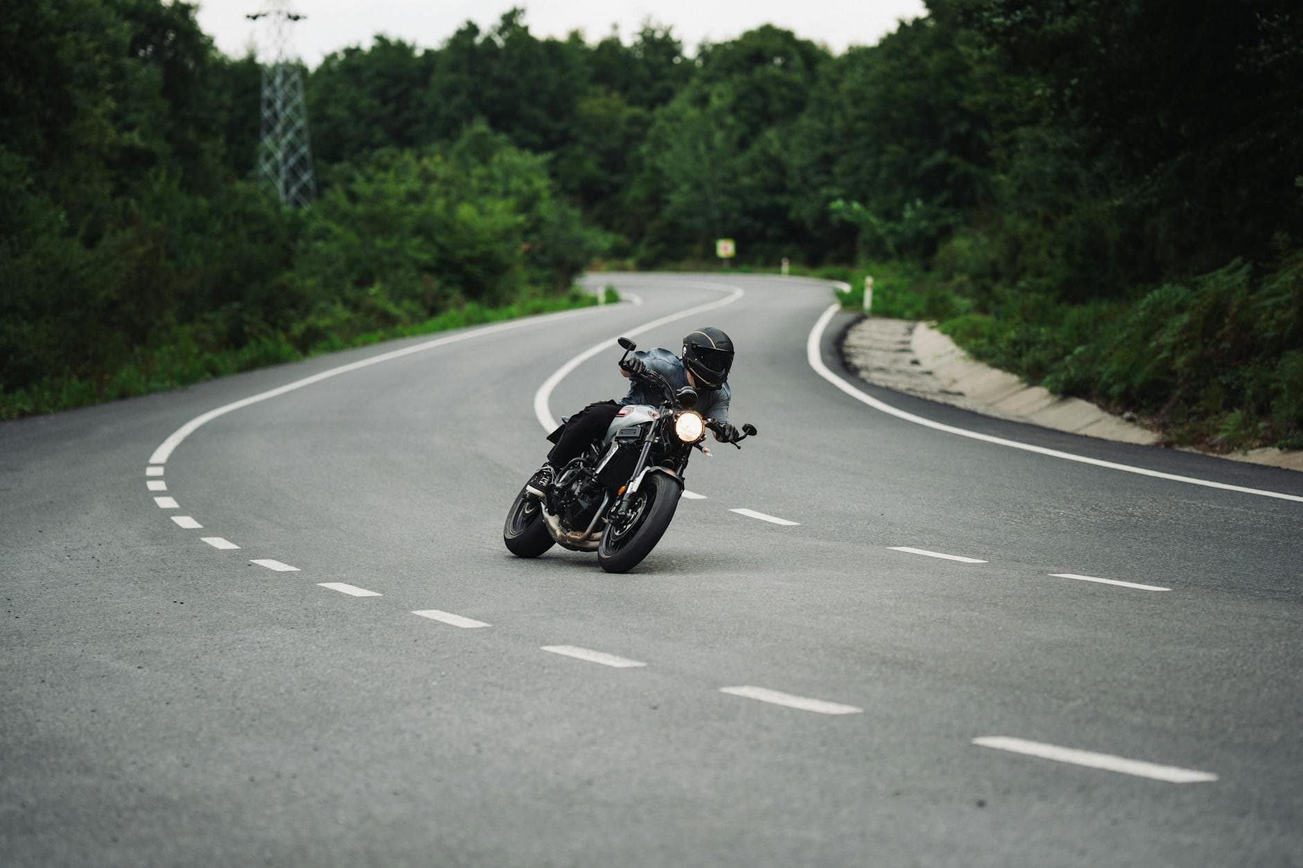 Motorcyclist in black gear maneuvering a curve on a scenic road surrounded by greenery.