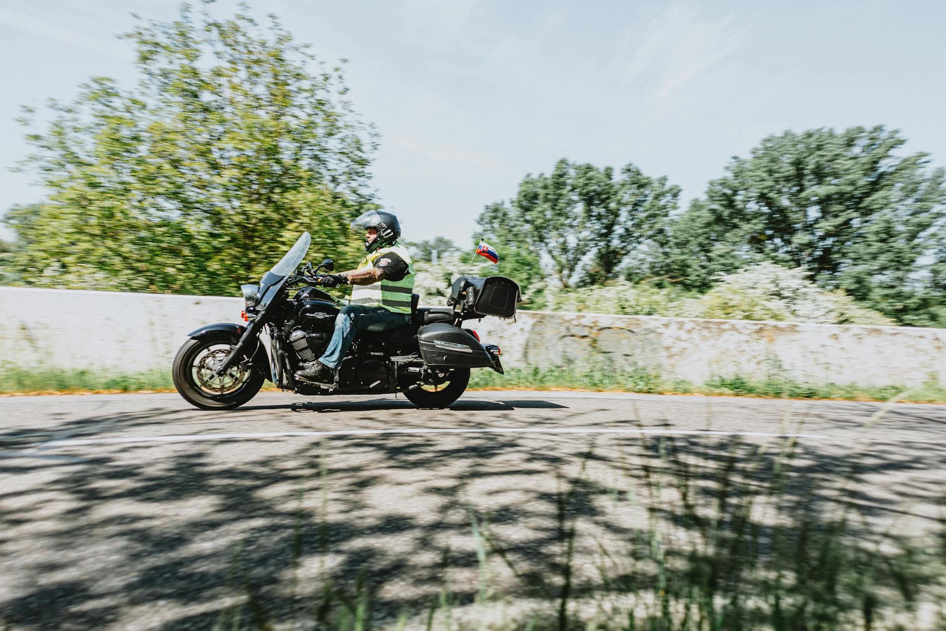 A motorcyclist rides down a sunny road with trees in the background, showcasing freedom and adventure.
