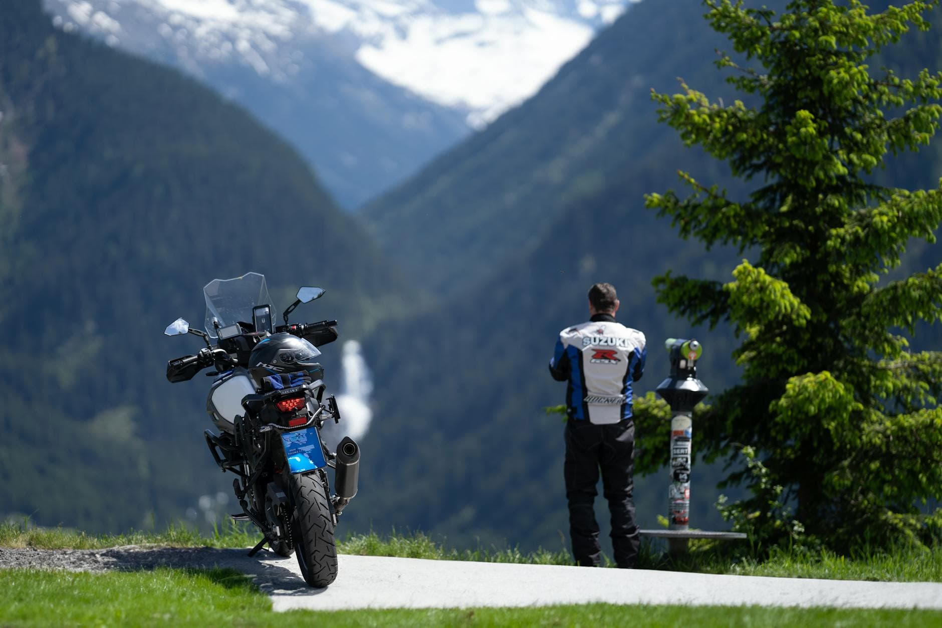 Person on motorcycle viewing scenic mountains with clear skies and lush greenery.