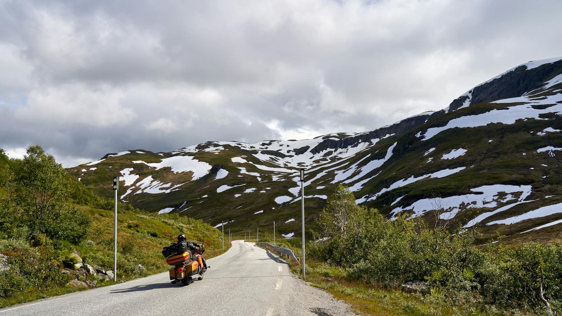 Motorcyclist rides through snow-capped mountains on a clear day, embracing adventure.