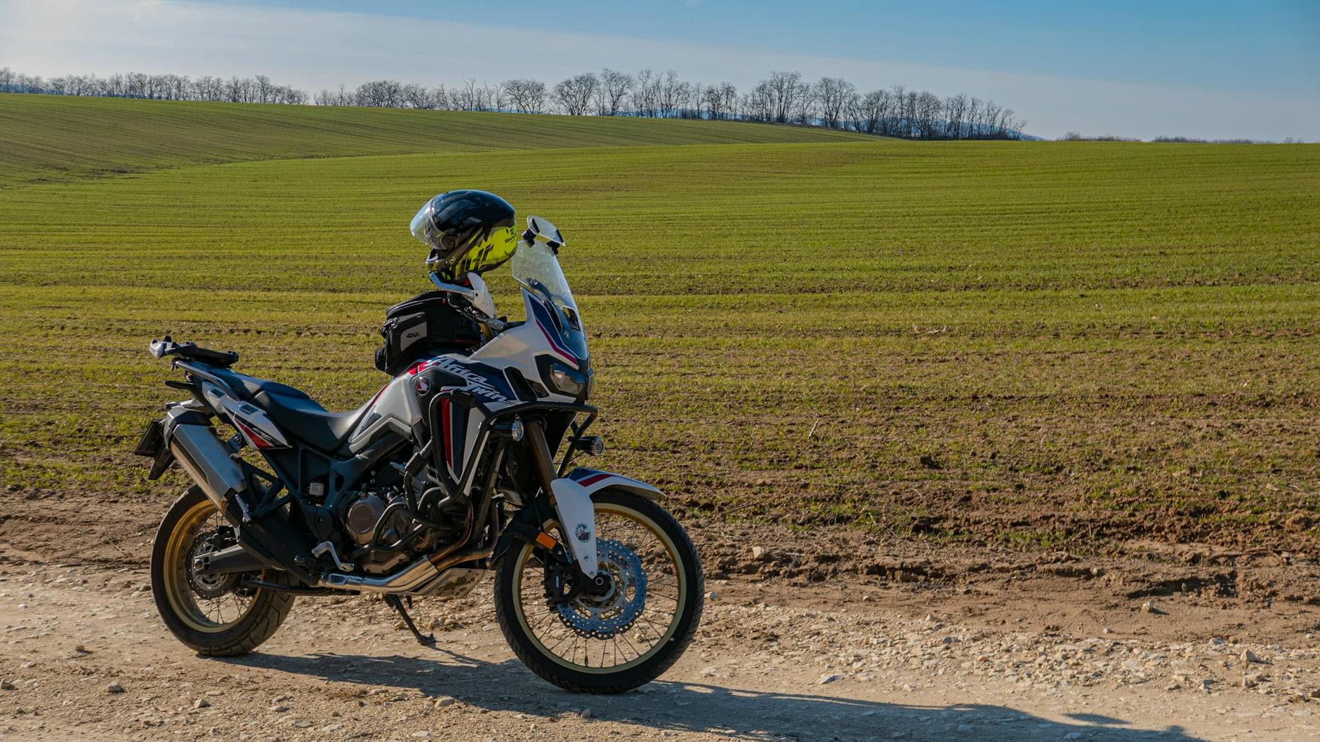 A sports motorcycle parked on a dirt road with lush green fields in Hungary.