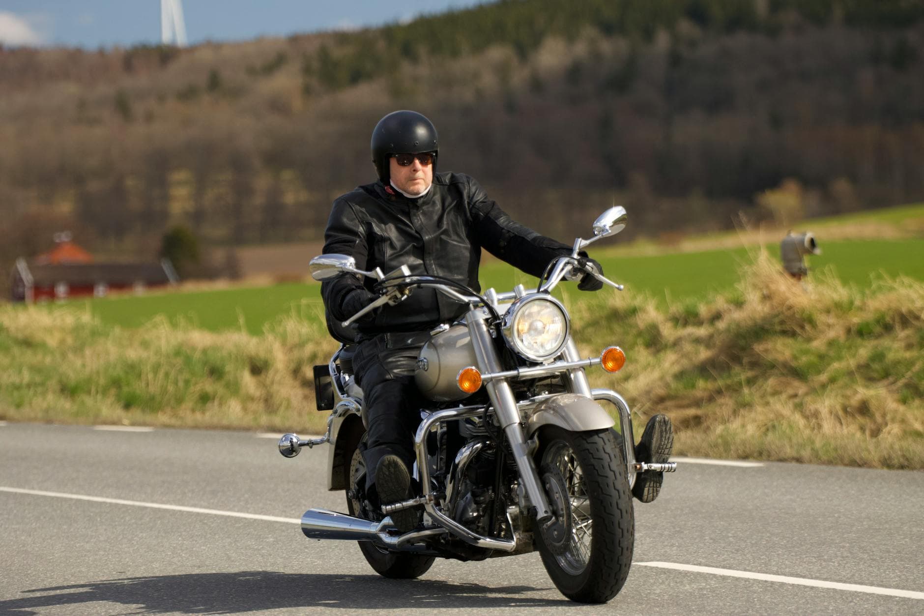 Biker in black leather outfit riding a classic motorcycle on a rural road in Sweden.