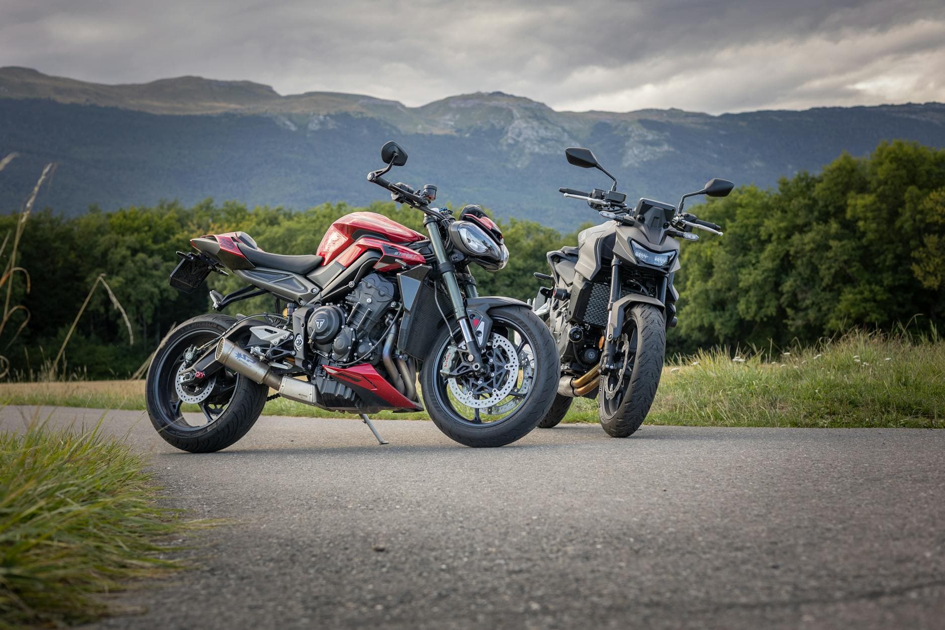 Two motorcycles parked on a rural road in Geneva, Switzerland with a scenic mountain backdrop.