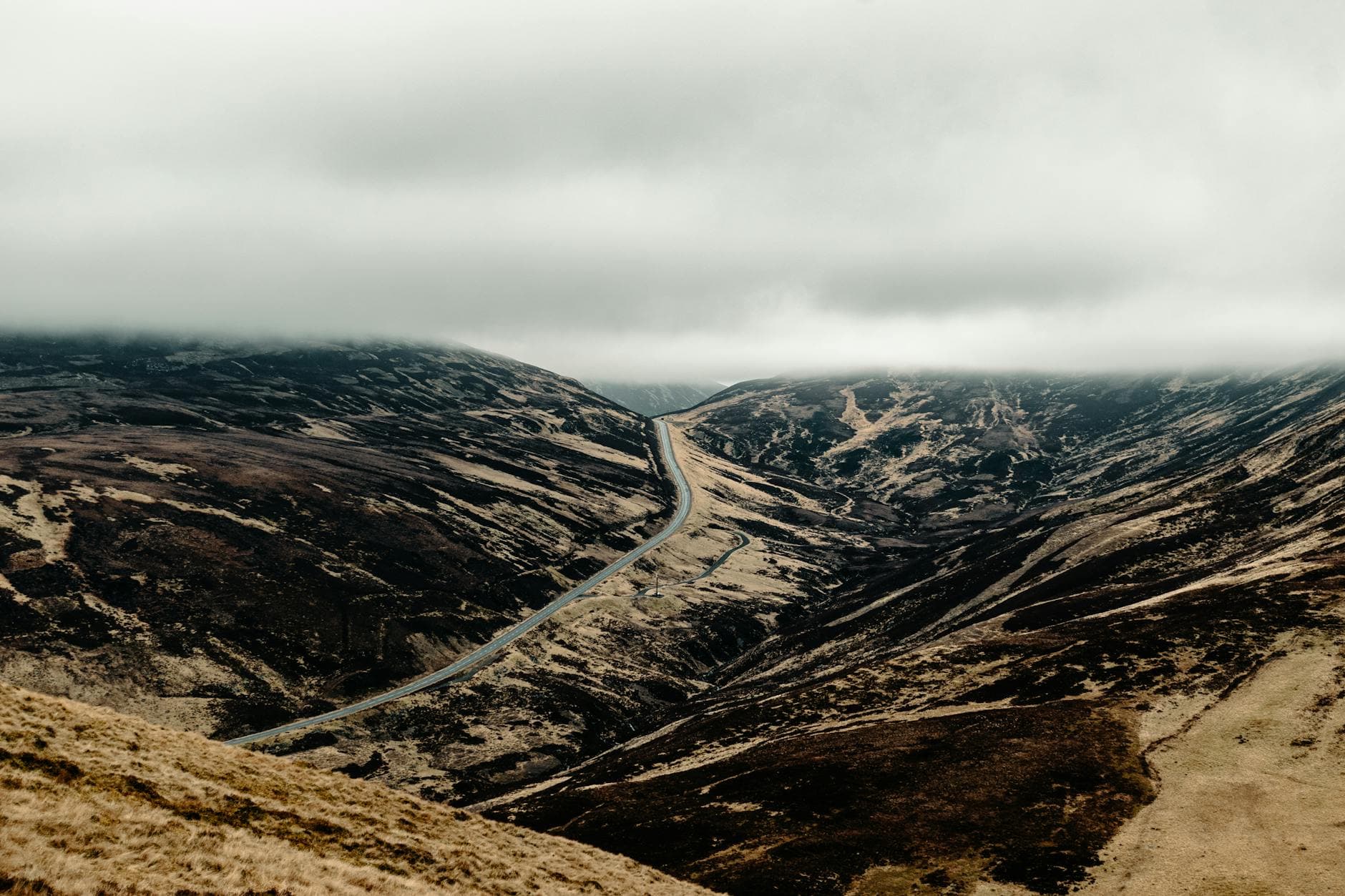 A breathtaking view of the Scottish Highlands with a winding road under moody, overcast skies.