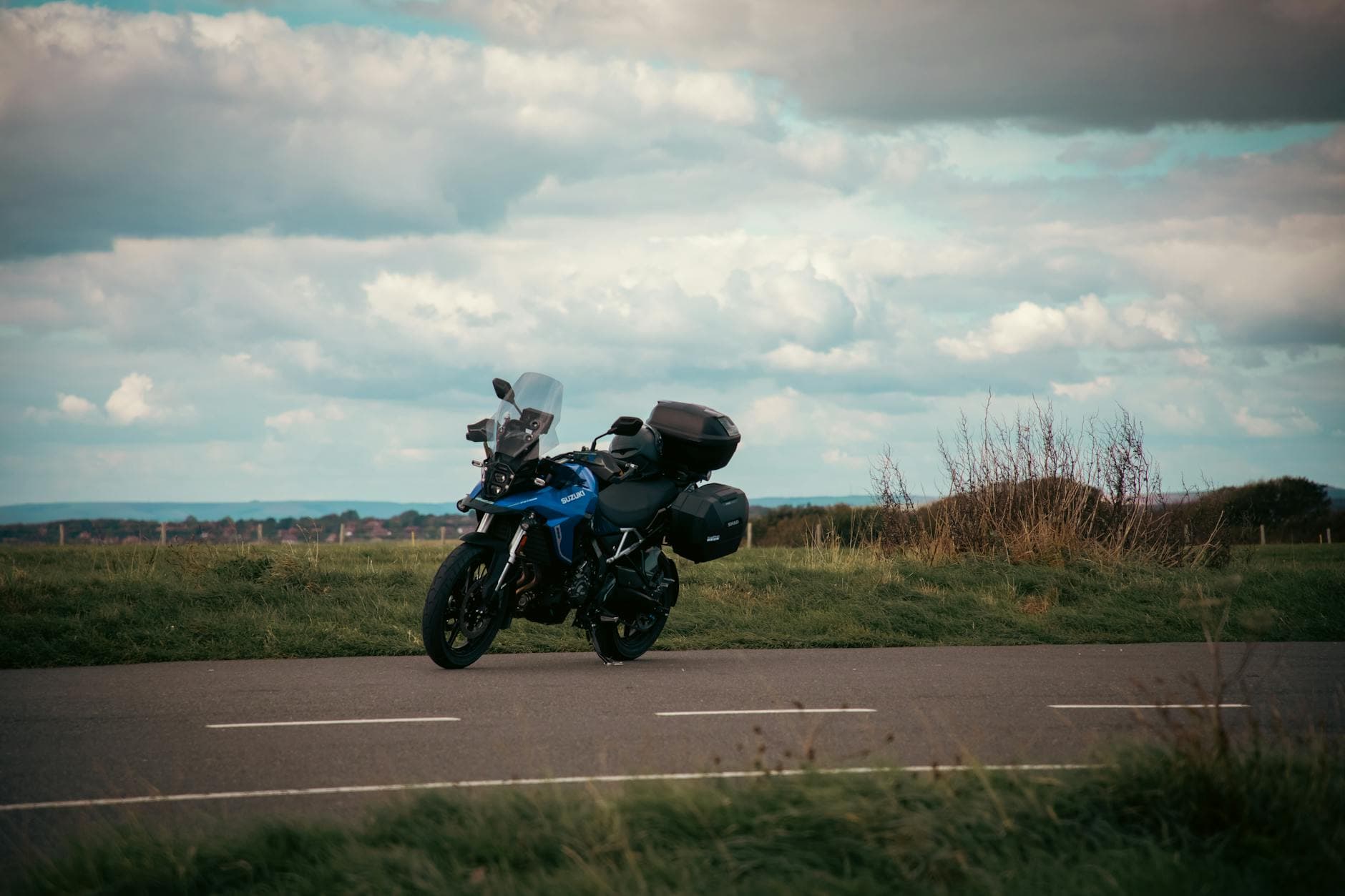 A blue motorcycle parked on a road in the English countryside under a cloudy sky.
